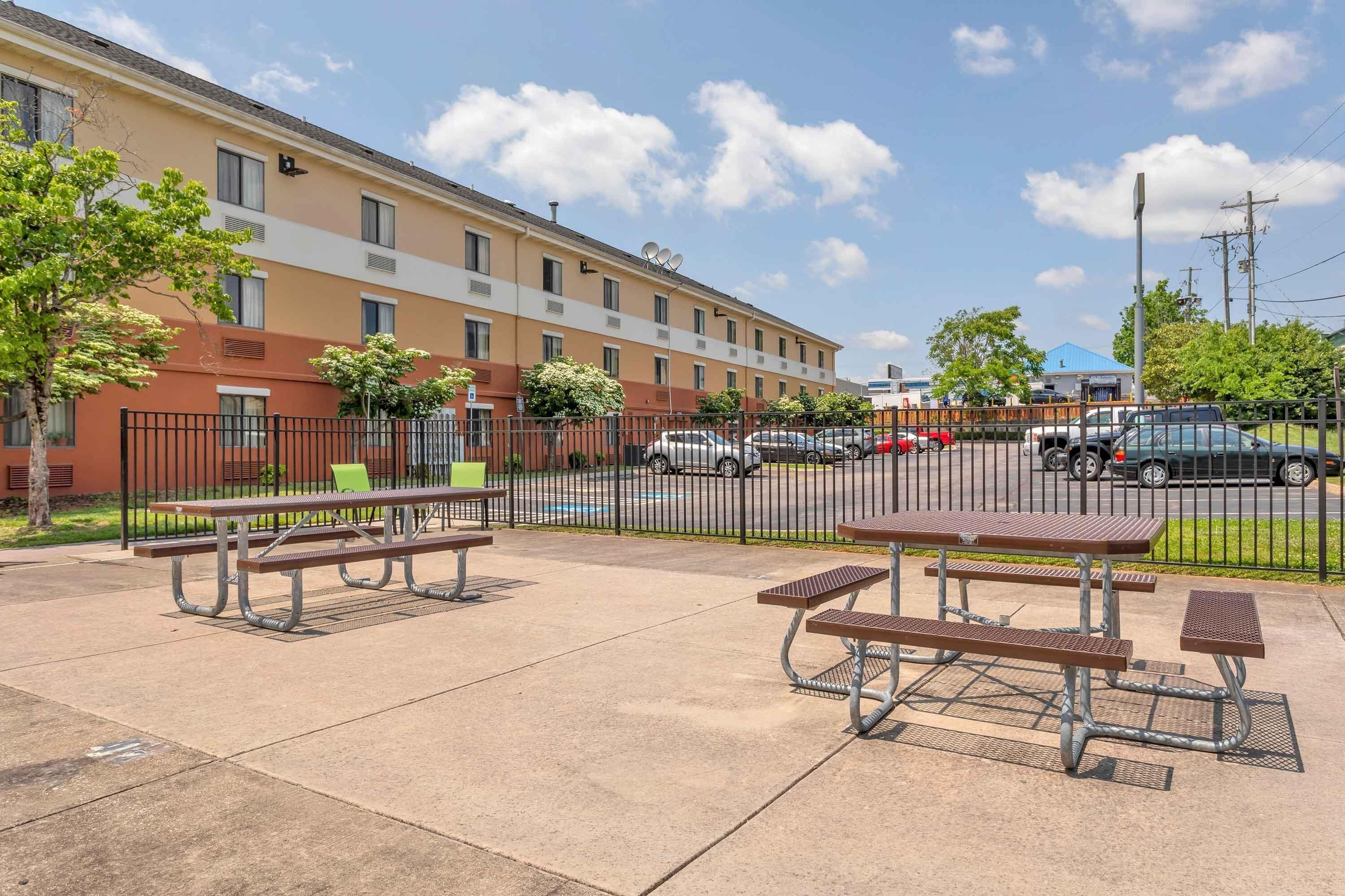 A multi-story building with a parking lot, picnic tables, and a fenced area.