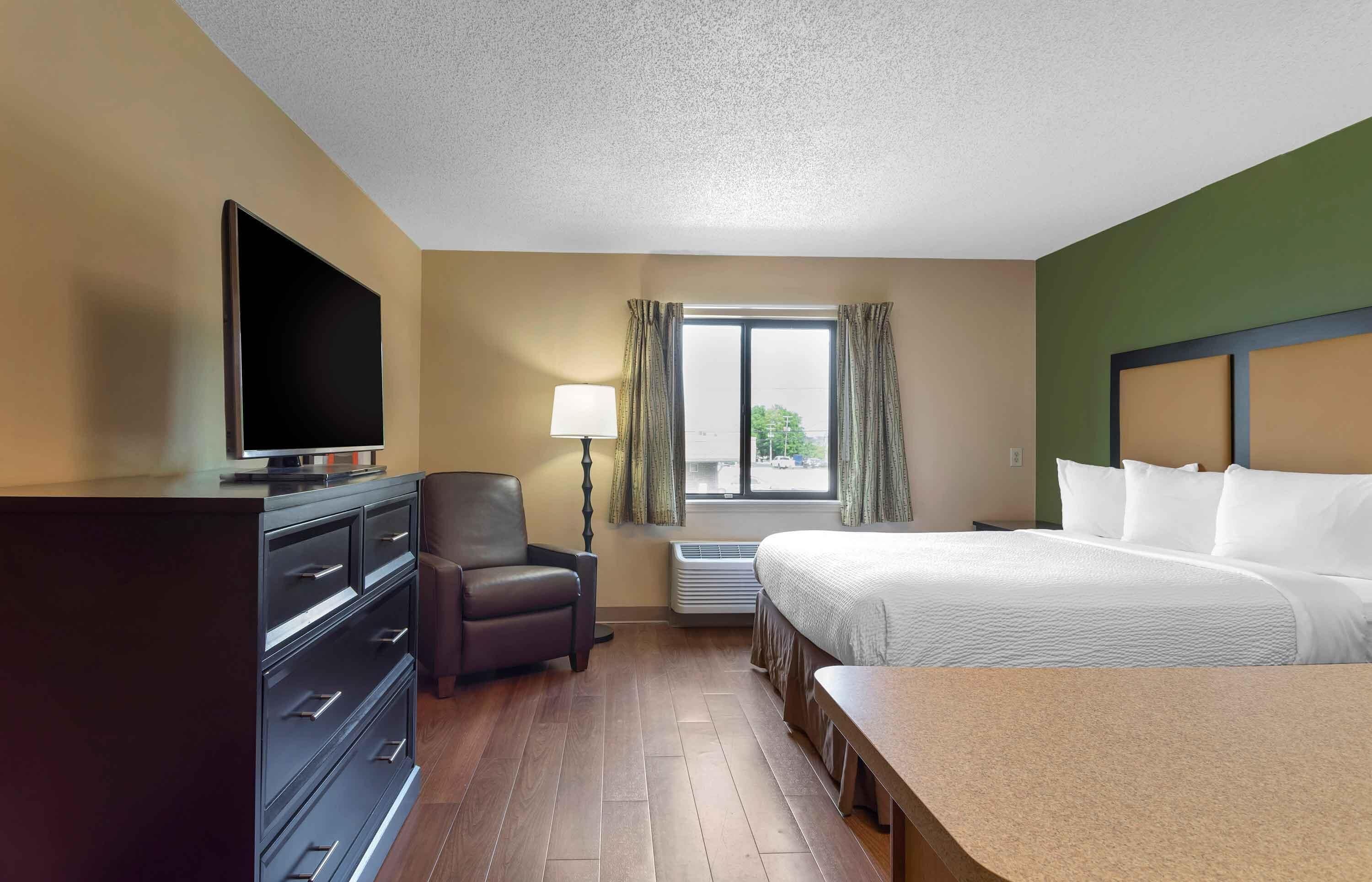 A hotel room with a bed, a desk, a chair, a TV, a lamp, and a window.