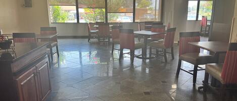A restaurant with hexagonal tiled flooring, wooden tables and chairs, and large windows offering a view of the outside.