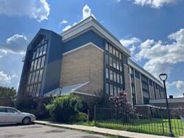 Un edificio moderno con amplios ventanales y techo plano, rodeado de vegetación y una cerca.