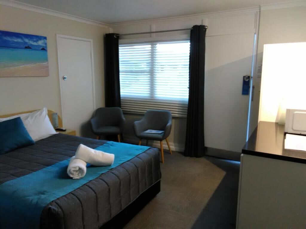 Ett hotellrum med en säng, två stolar, ett skrivbord och ett fönster med gardiner.