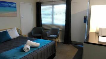 Ett hotellrum med en säng, två stolar, ett skrivbord och ett fönster med gardiner.