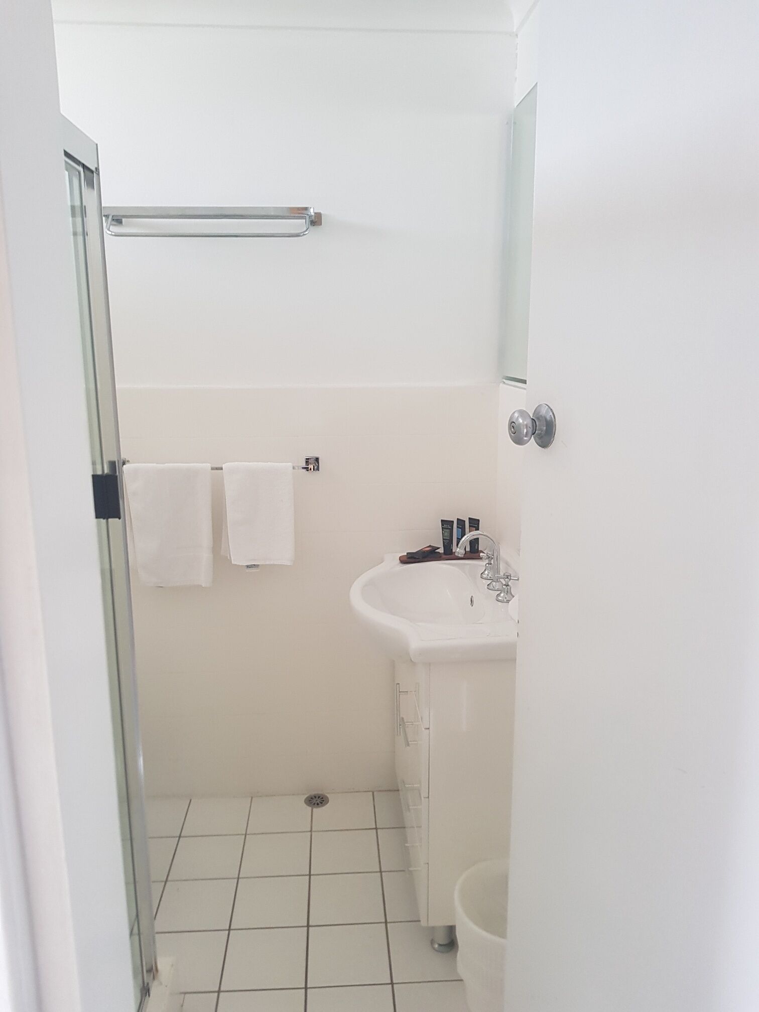 A small, clean bathroom with a white sink, a mirror, and a glass shower enclosure.
