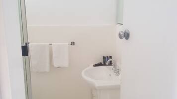A small, clean bathroom with a white sink, a mirror, and a glass shower enclosure.