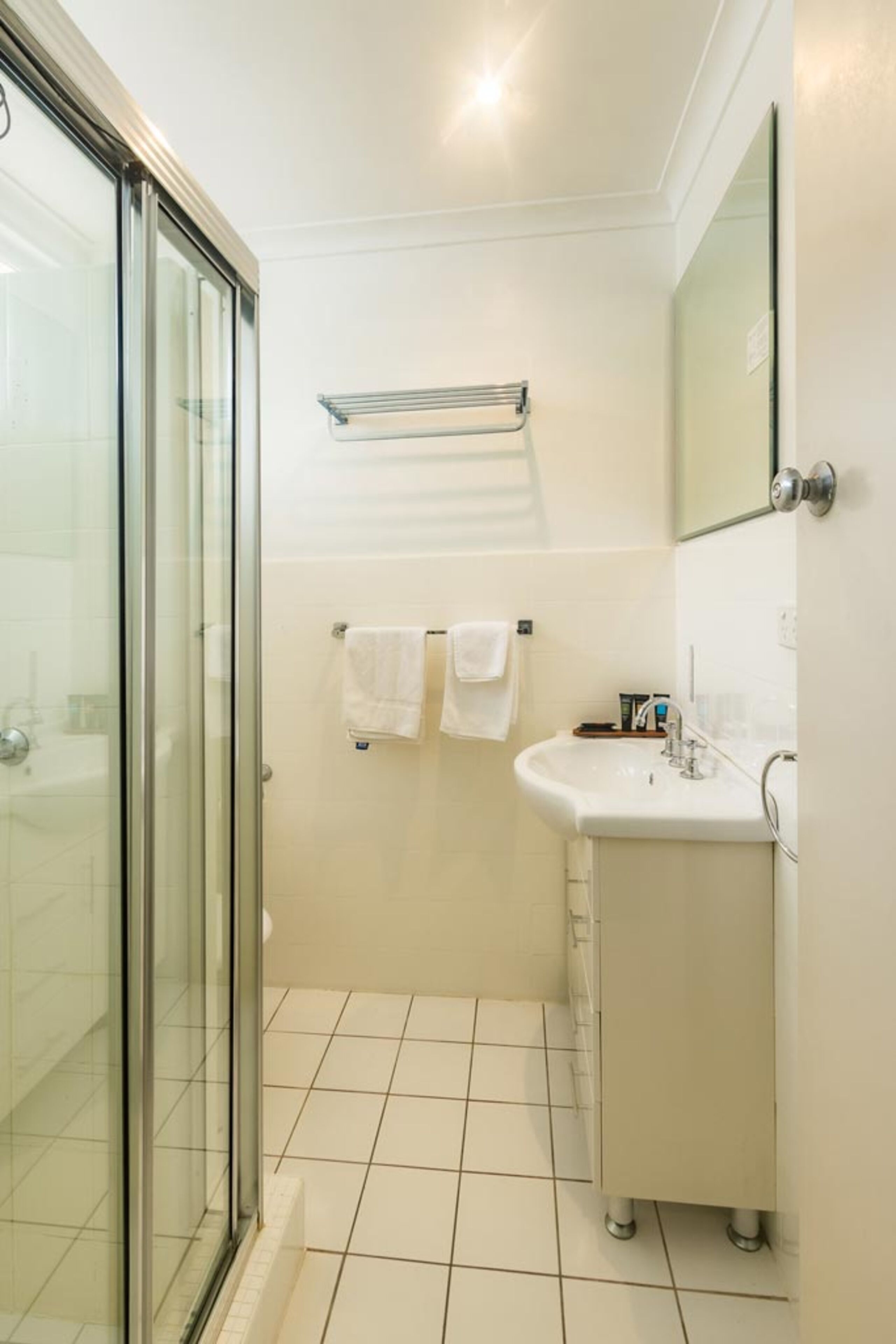 A bathroom with a glass shower enclosure, a sink with a mirror, and two towels hanging on a rack.