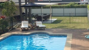 Una piscina con sillas de descanso y una mesa, rodeada por una valla y vegetación.