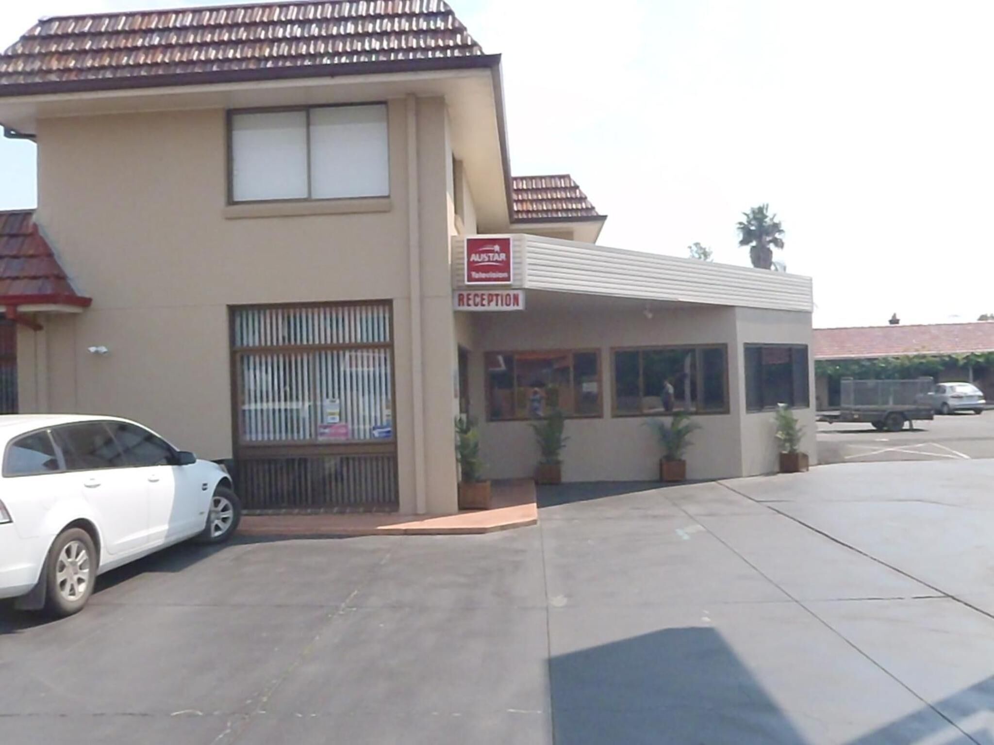 A building with a reception area, a car parked in front, and a truck in the background.
