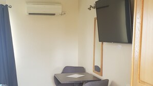 Habitación compacta con una televisión de pantalla plana montada en la pared, una mesita con sillas y un sofá.