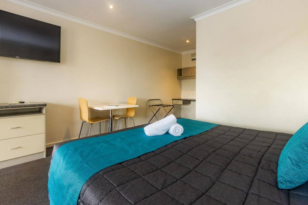 A hotel room with a bed, a desk, a chair, and a television on the wall.