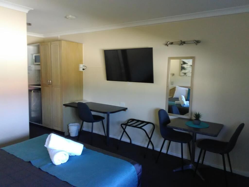 Habitación de hotel con cama, escritorio, dos sillas, televisor, espejo y kitchenette.