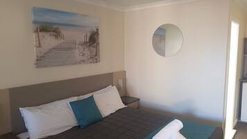 Una camera d'albergo con un letto, un dipinto di una spiaggia, uno specchio tondo e un letto rifatto con un asciugamano.