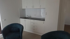Una cocina con gabinetes blancos, una encimera negra y dos sillas azul oscuro.