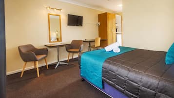 A hotel room with a bed, two chairs, a desk, a television, and a mirror.