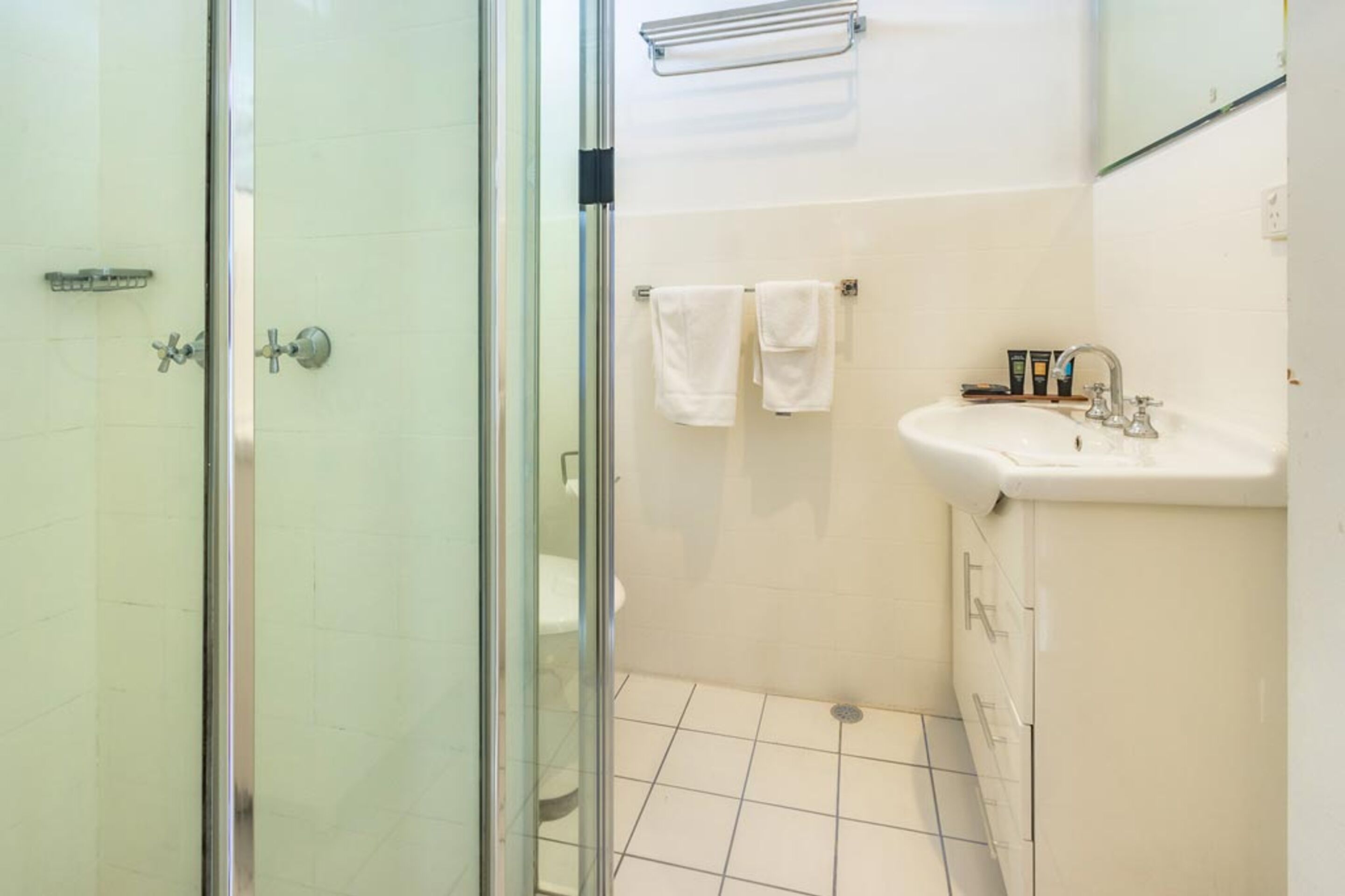 Un bagno con box doccia in vetro, un lavabo con specchio e due asciugamani bianchi su un portasciugamani.