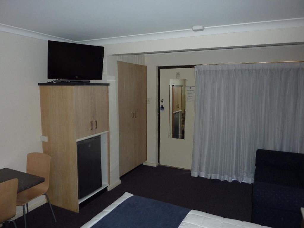 Quarto de hotel com cama, televisão sobre um móvel, escrivaninha e porta que dá para um banheiro.