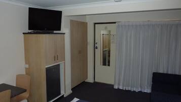 Quarto de hotel com cama, televisão sobre um móvel, escrivaninha e porta que dá para um banheiro.