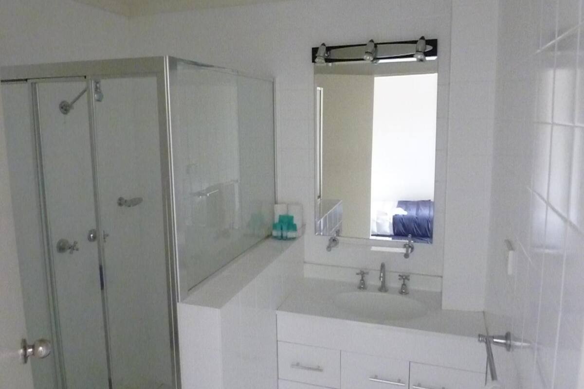 A bathroom with a glass shower enclosure, a sink with a mirror above it, and a vanity with drawers.