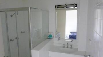 Une salle de bain avec une douche à parois de verre, un lavabo avec un miroir au-dessus et un meuble-lavabo avec des tiroirs.