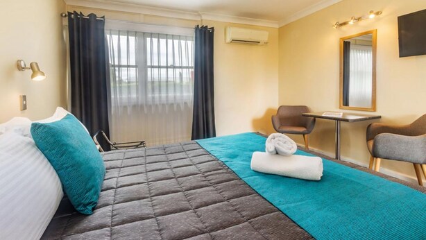 Habitación de hotel con cama, escritorio, silla y un amplio ventanal con cortinas.