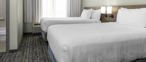A hotel room with two beds, a large window with curtains, a wall-mounted light fixture, and a carpeted floor.