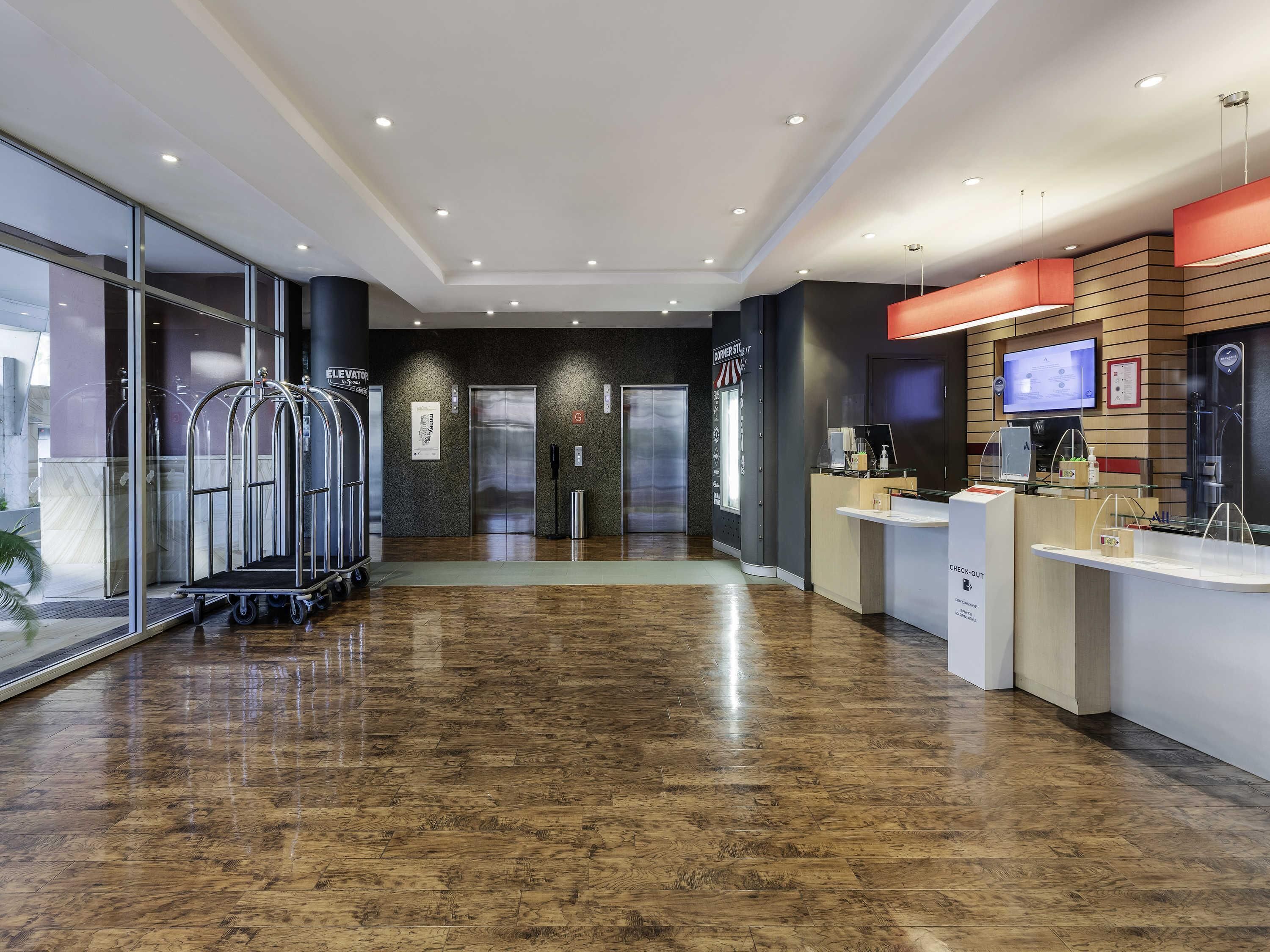 A modern hotel lobby with a reception desk, elevators, and a glass entrance.