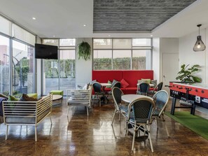 A spacious indoor area with a red sofa, multiple chairs, a foosball table, and a TV mounted on the wall. - ibis Sydney Darling Harbour (Sydney)