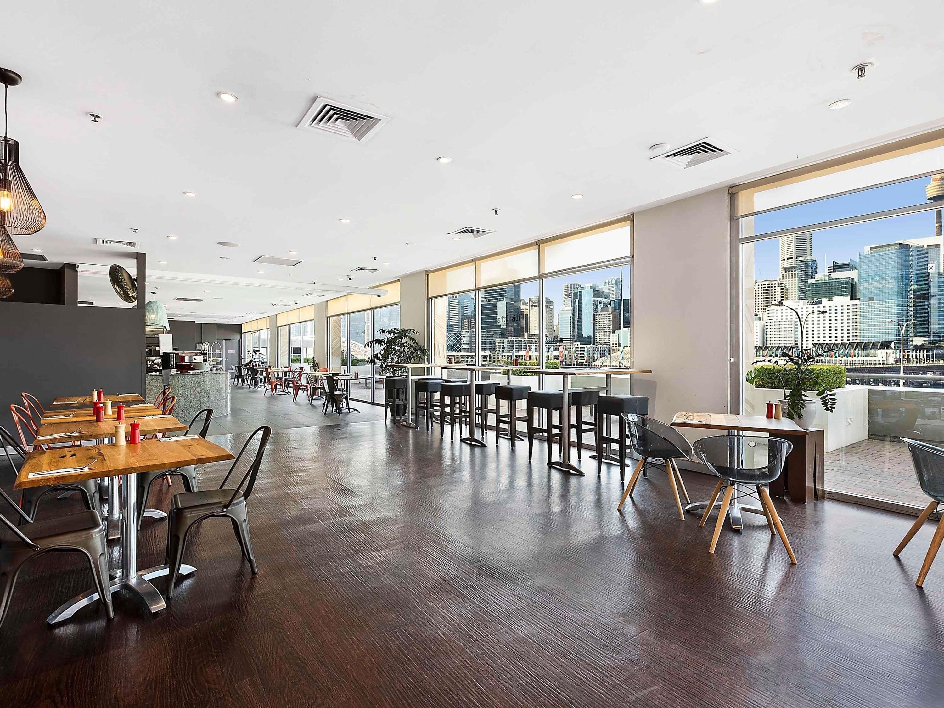 A spacious dining area with high ceilings, large windows offering city views, and modern furniture.