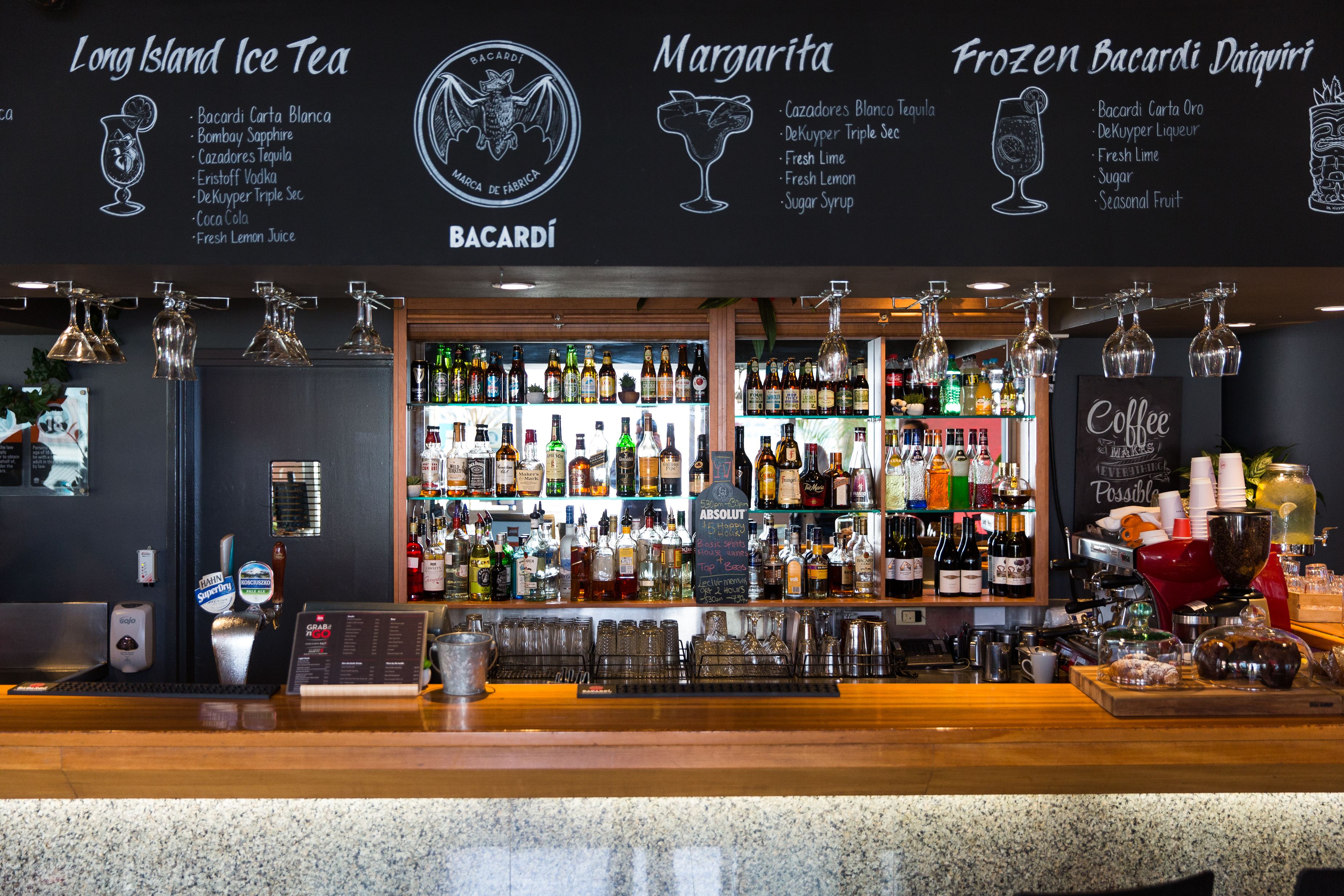 A bar area with a variety of liquor bottles, a selection of glasses, and a menu board listing drinks like Long Island Ice Tea and Margarita.