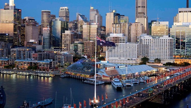 A city skyline with modern high-rise buildings, a waterfront promenade, and a prominent hotel with a distinctive roof structure. - ibis Sydney Darling Harbour (Sydney)