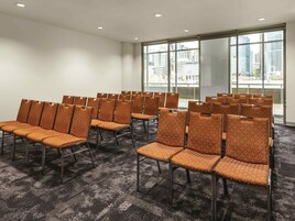 A conference room with rows of orange chairs, large windows with a city view, and a carpeted floor.