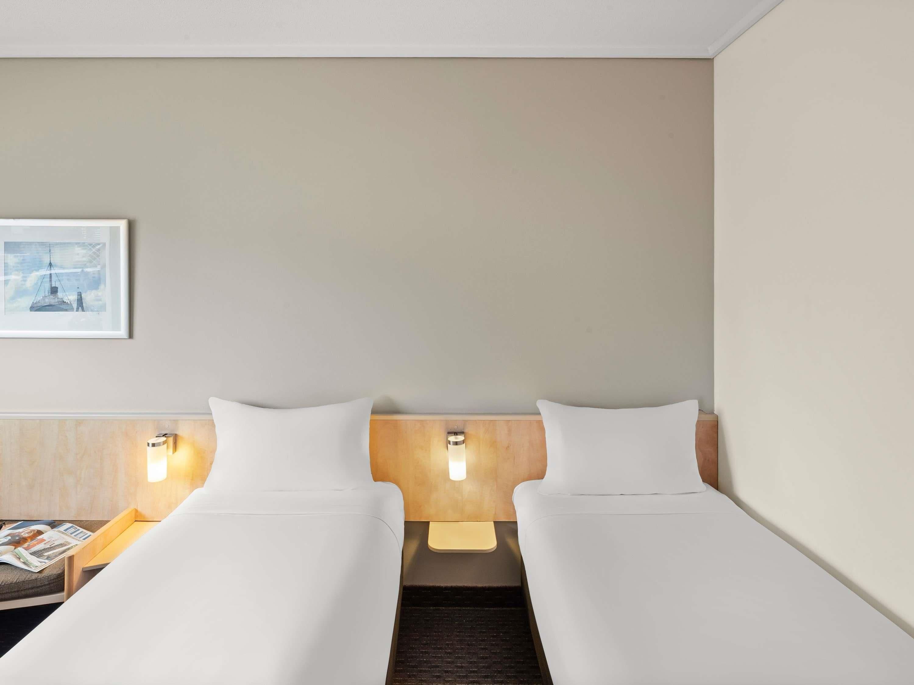 A hotel room with two beds, a nightstand, a lamp, and a framed picture on the wall.