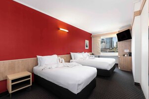 Habitación de hotel con dos camas, una mesita de noche pequeña, un televisor y vista a la ciudad.