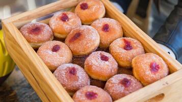 A wooden tray holding several round pastries with a dusting of sugar and a red filling, placed on a barrel.