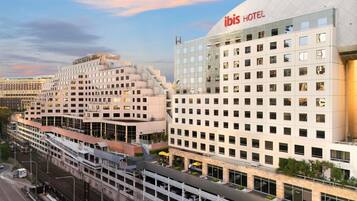 A modern hotel with a prominent "ibis HOTEL" sign, a multi-story structure with a flat roof, and a parking area with a covered walkway.