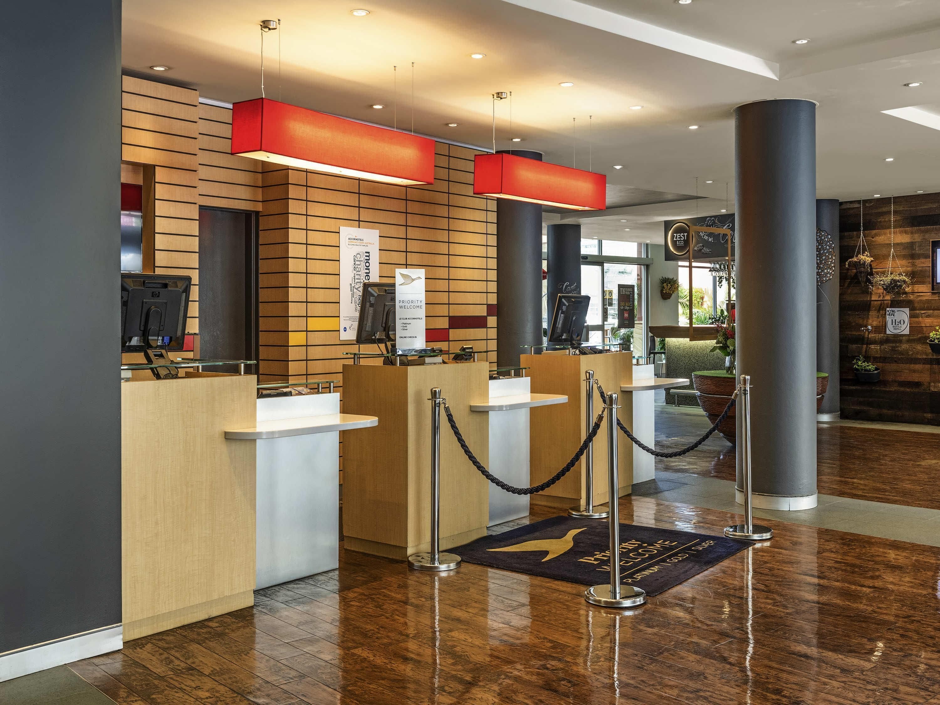 Una moderna zona de recepción con paneles de madera, un mostrador y un quiosco de información digital.