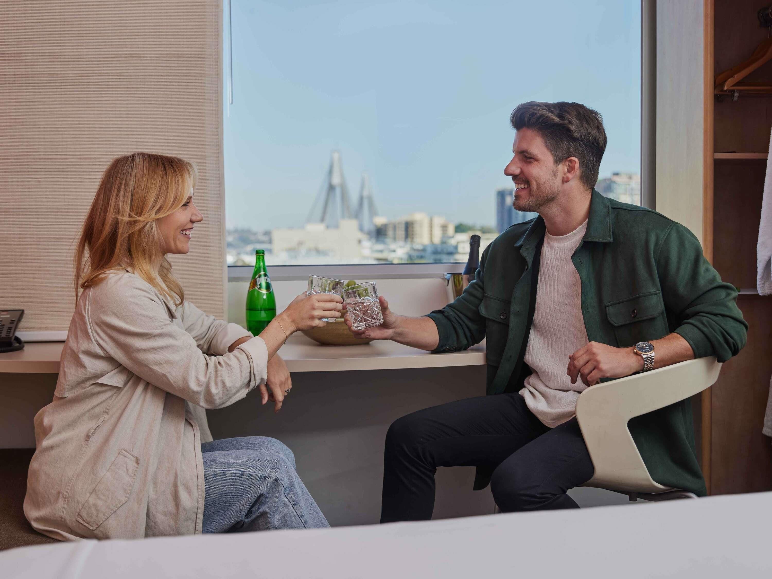 Two people sitting at a table with a city view, a bottle, and a glass.