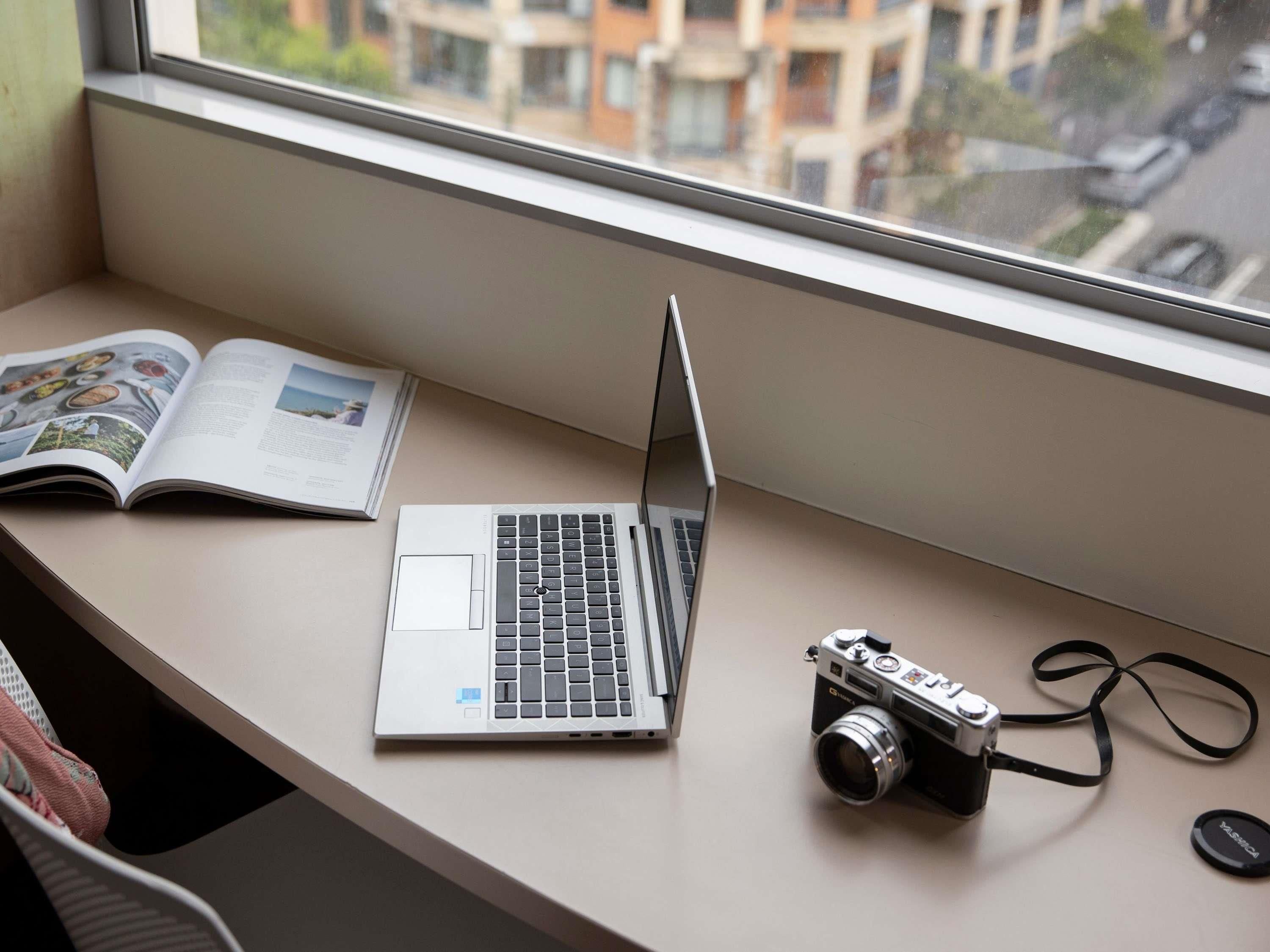 A laptop and a camera on a window sill with a book beside it.