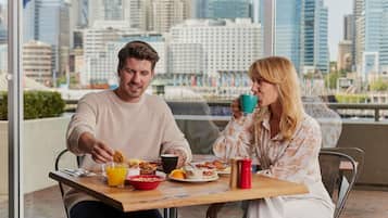 Two people sitting at a table with breakfast items, a city view, and a sign reading 'RESTAURANT.'