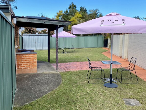 A patio area with a brick wall, a pergola, and two tables with chairs.