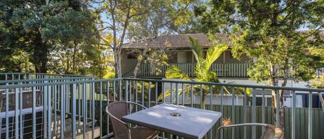 A balcony with a table and two chairs, surrounded by a metal railing and trees.