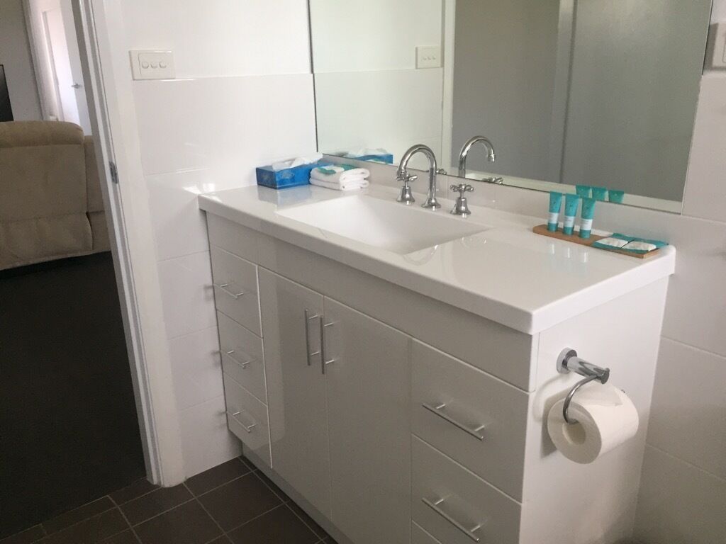 A bathroom with a white sink, two faucets, a mirror, and a toilet paper holder.