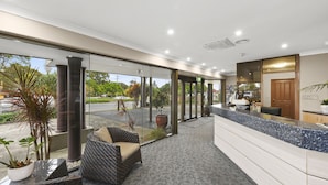 A reception area with a counter, seating, and large windows. - Macquarie Barracks Motor Inn (Port Macquarie)