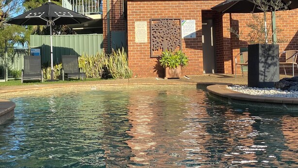 A pool area with a brick building, a balcony, and outdoor seating. - Macquarie Barracks Motor Inn (Port Macquarie)