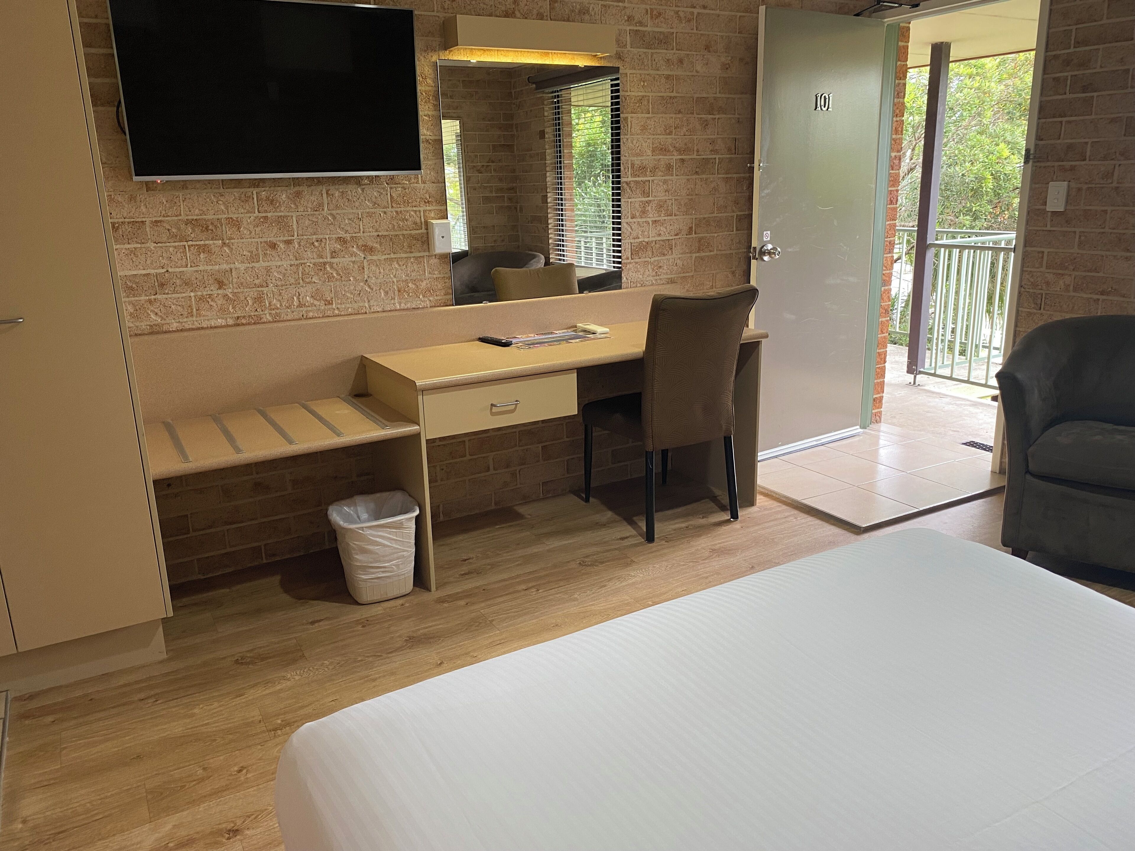 Une chambre d’hôtel comprenant un lit, un bureau avec une chaise, un téléviseur fixé au mur et une porte donnant sur un balcon extérieur.