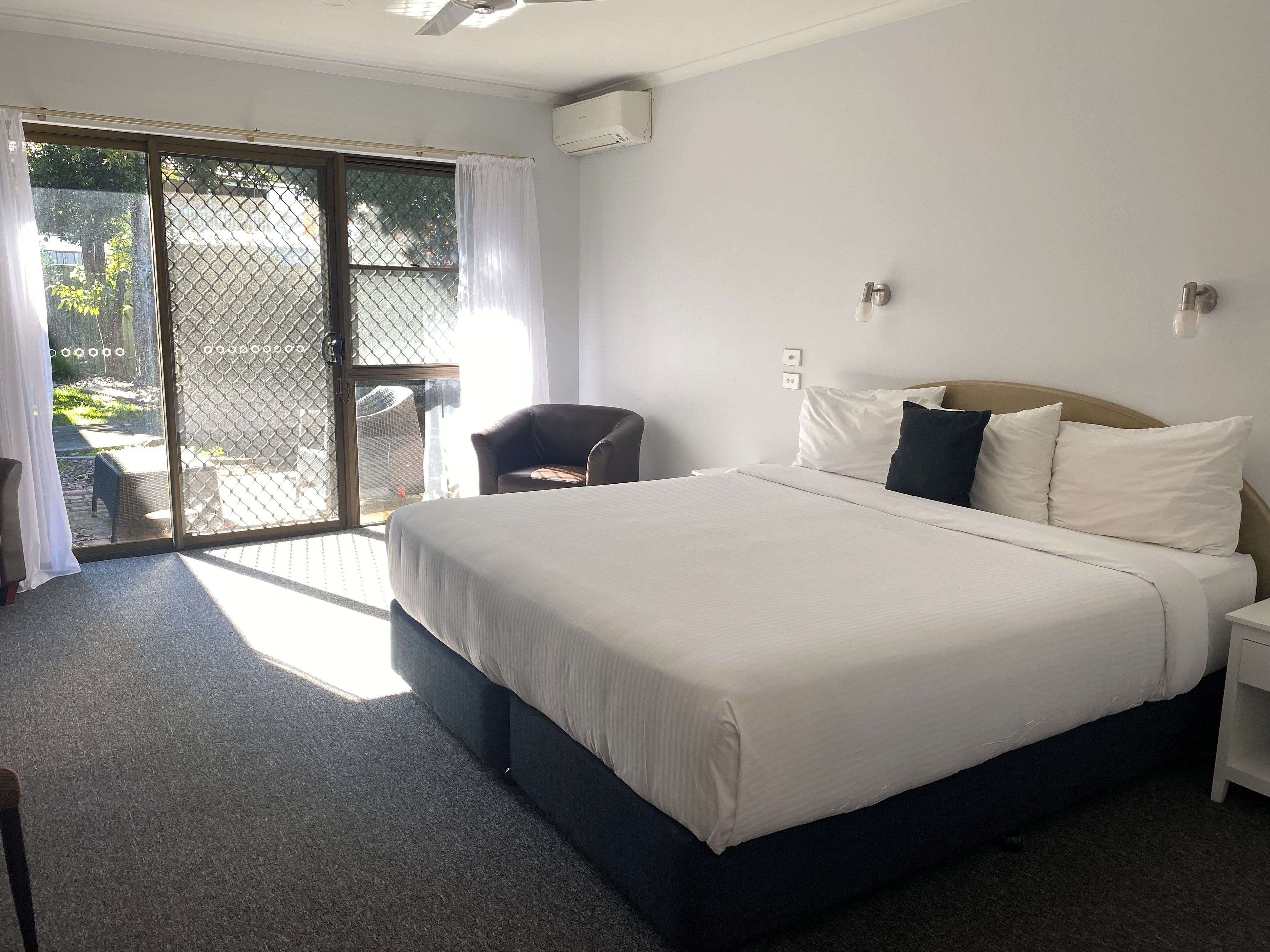 Quarto de hotel com uma cama grande, uma cadeira, uma mesinha e uma porta de vidro deslizante que dá para uma área externa.