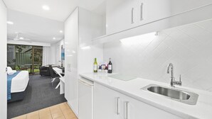 A modern kitchen with white cabinets, a stainless steel sink, and a dining area with a table and chairs. - Macquarie Barracks Motor Inn (Port Macquarie)