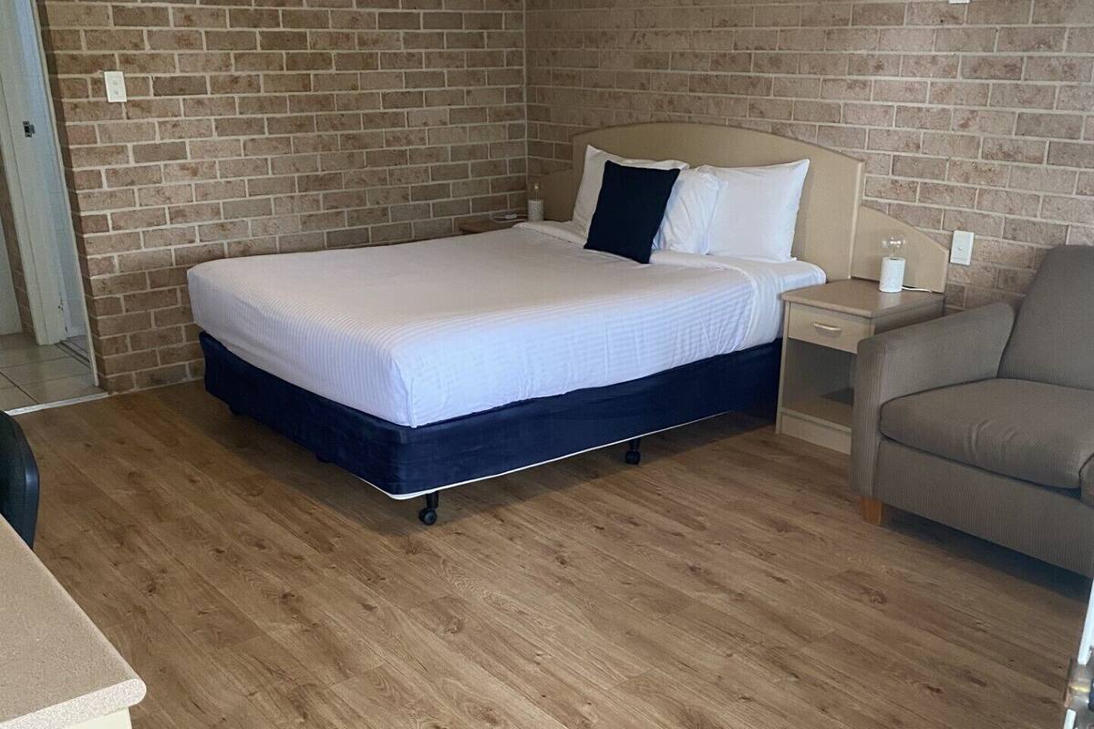 Quarto com uma cama, mesa de cabeceira, cadeira e parede de tijolos.