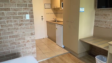 A compact room with a kitchenette, a bed, and a trash bin.