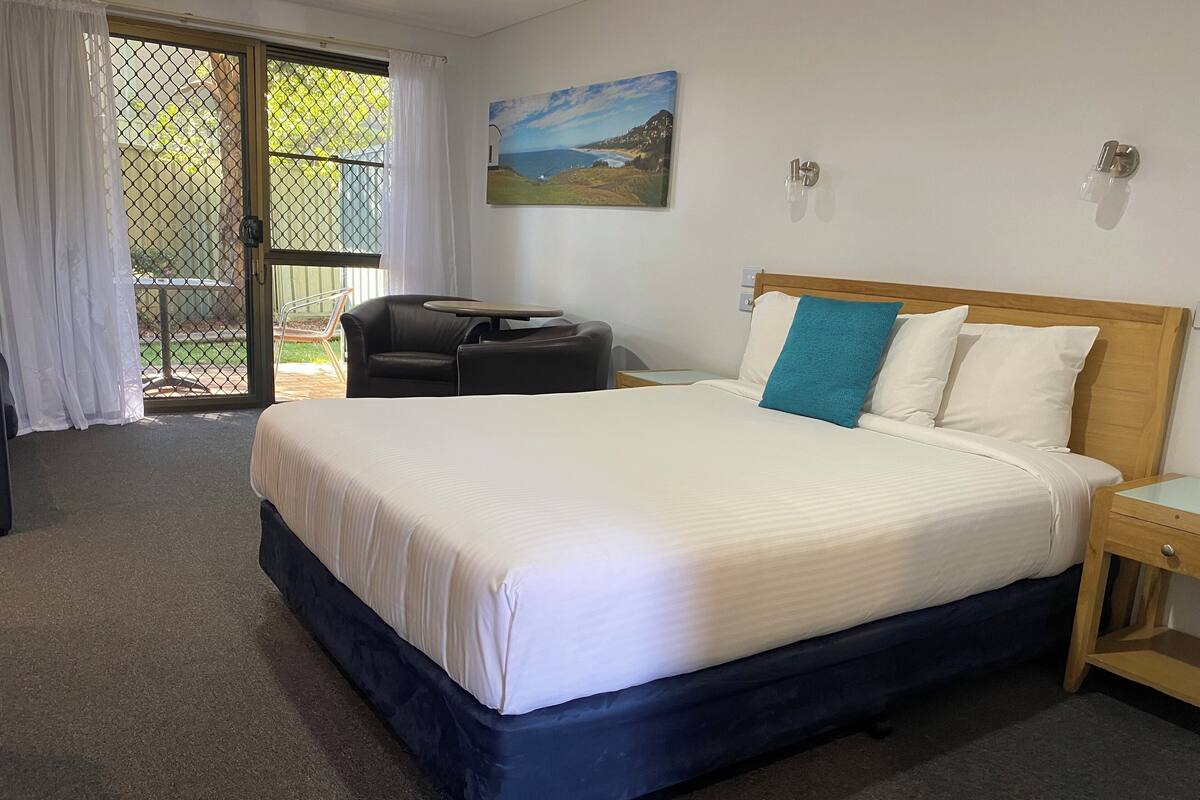 Quarto de hotel com uma cama grande, uma cadeira, uma mesinha e um quadro na parede.