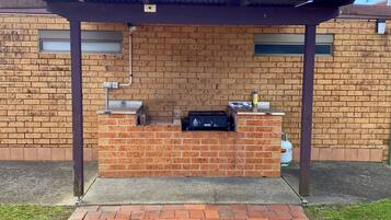 Un área de parrillada de ladrillo con una parrilla de metal, un tanque de gas y una lata de cerveza sobre el mostrador.